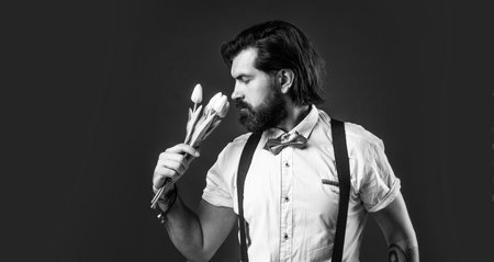 handsome hipster hold tulip bouquet. fathers day. mature retro man. bearded man in suspenders smell flowers. brutal guy ready for romantic date. elegant male with floral presentの写真素材