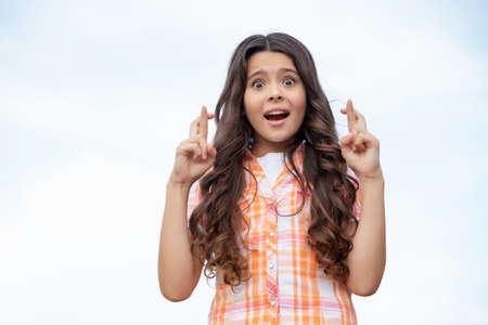 Terrified teen girl keeping fingers crossed sky background, copy spaceの写真素材