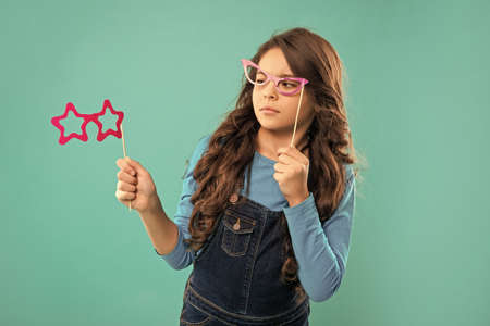 unpleased kid with long curly hair on blue background. funny child with glasses.