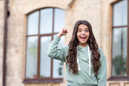 Shocked teen girl making winning gesture in casual hoodie blurry outdoors