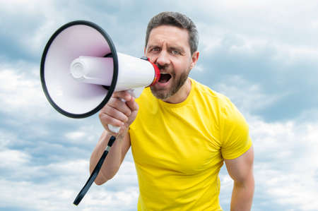 man in yellow shirt shout news in loudspeaker on sky backgroundの写真素材