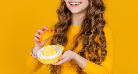 cropped view of girl holding orange and juicer on yellow background