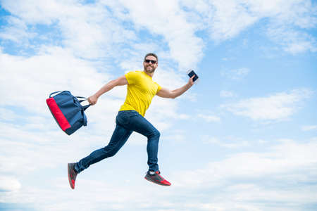 Energetic man running with travel bag midair sky background, vacation