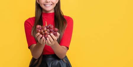 smiling kid hold bunch of grapes on yellow background