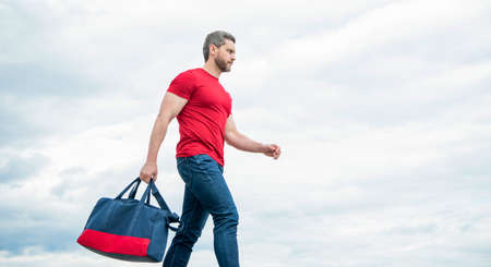 Active man walking with sporty bag sky background, copy space
