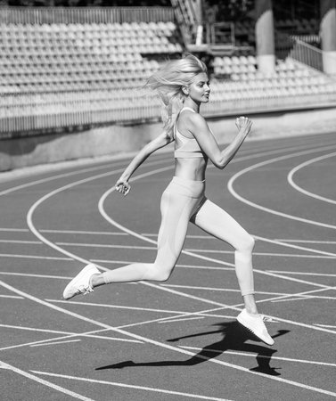 fit lady in fitness wear running on stadium racetrack while sport workout, staminaの写真素材