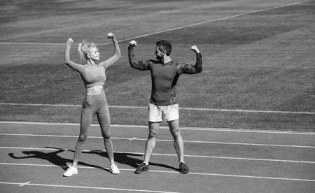fitness woman and man celebrate success or show biceps muscles together on outdoor stadium racetrack...