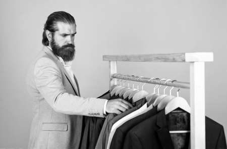 well groomed man in wedding formalwear has beard choose jacket in wardrobe, fashionの写真素材
