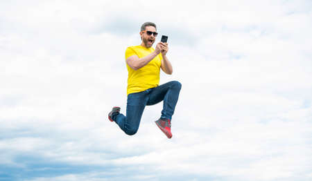 man jumping and chatting on phone on sky backgroundの写真素材
