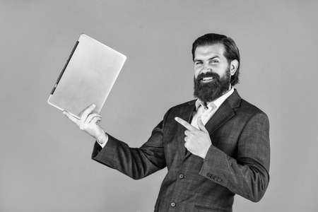 happy caucasian bearded hipster with computer. male employee holding finance report and researches in coworking space on laptop. new technology in modern business lieの写真素材