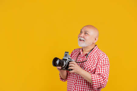 happy old man with retro photo camera on yellow baqckground. copy space