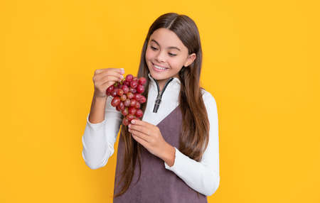 positive child hold fresh grapes bunch on yellow background