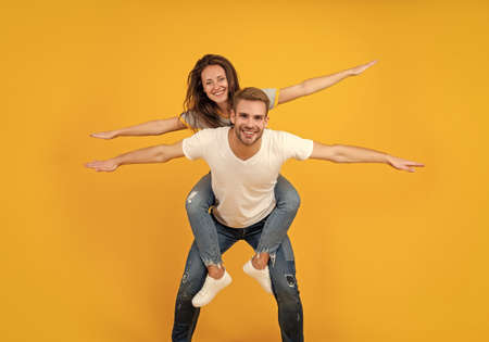 Happy playful woman and man pretend flying doing piggyback ride yellow background, funの写真素材