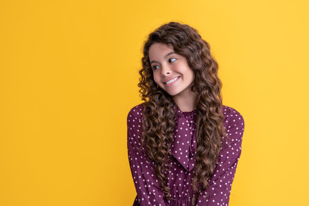 cheerful child with long brunette frizz hair on yellow backgroundの写真素材