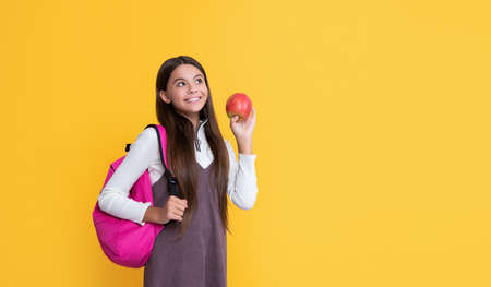 positive child with school backpack and apple on yellow backgroundの写真素材