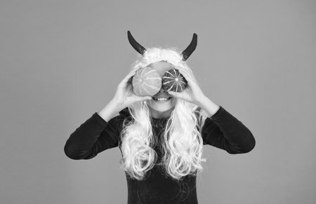 watching pumpkins. kid has white hair hold pumpkin. jack o lantern. carnival costume party. trick or treat. celebrate the holidays. childhood. happy halloween devil girl. teenage child in imp hornsの写真素材