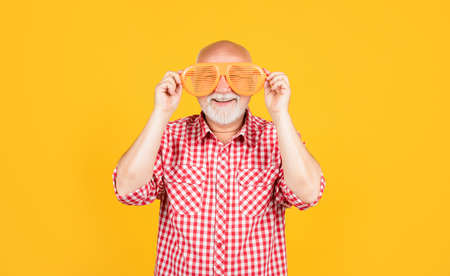 smiling old man in checkered shirt with party glasses on yellow backgroundの写真素材