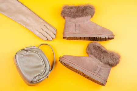 pair of fashionable winter ugg boots leather gloves and bag on yellow background, fashion accessory