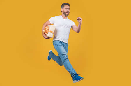 Energetic courier guy running with present box in midair yellow background. Courier service.