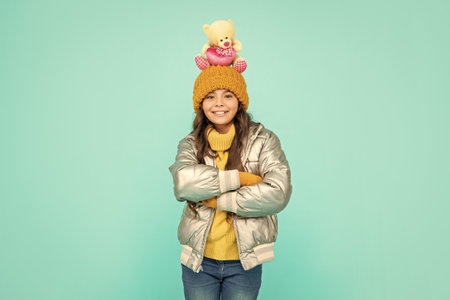 happy teen girl with toy bear crossed hands. child wear warm clothes on blue background.