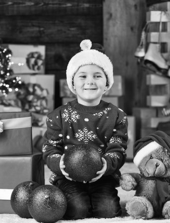 Colorful fun. happy new year. happy child santa hat. son ready to celebrate winter holidays. small boy excited with present. kid hold decorative ball. bear toy gift for at xmas. merry christmasの写真素材