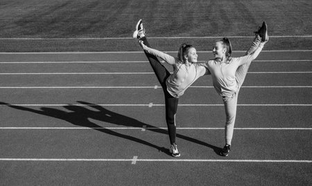 Keeping those muscles flexible. teen girls warming up on stadium. kids in sportswear stretching. children do exercise. healthy childhood. workout on fresh air outdoor. confident flexible gymnastsの写真素材