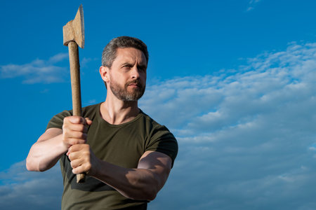 man threaten with axe. caucasian man hold ax. brutal man on sky background with copy space