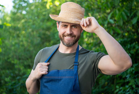 Happy gardener man in gardening apron tipping hat and smiling natural outdoorsの写真素材