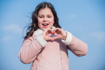 child with happy face show heart gesture on sky background