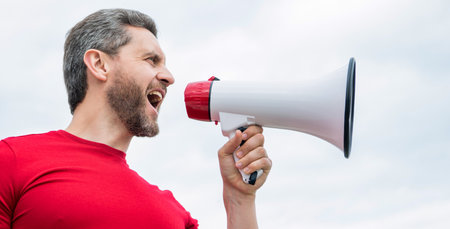 man in red shirt shout in loudspeaker on sky background. propagandaの写真素材