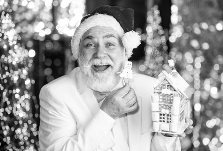 Christmas house and snowman toy. Buy new home. Real estate. Senior businessman in santa claus hat. Christmas deal. Christmas decor. Gingerbread. Mortgage concept. Businessman hold little houseの写真素材