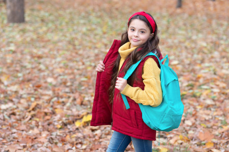 Schoolgirl carrying school bag on autumnal day. Happy girl back to school in autumnの写真素材