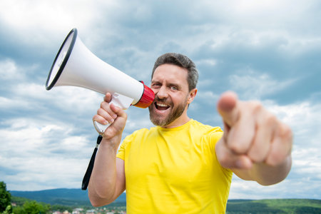 man in yellow shirt shout in loudspeaker on sky background. announceの写真素材
