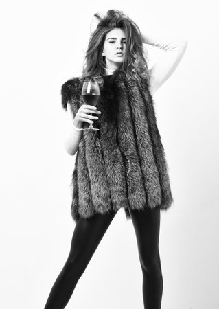 Fashionable lady likes luxury. Girl enjoy luxury lifestyle attributes. Fashion model long hair fur coat or vest hold wineglass. Woman drink wine wear luxury fur clothing. Luxury lifestyle conceptの写真素材