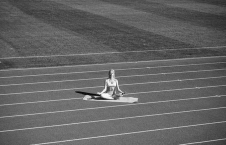 fit lady in fitness wear meditating on stadium after sport workout, yogaの写真素材