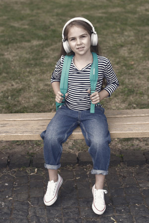 Modern education. Small child wear headphones summer outdoors. Little girl listen to music. Modern technology in education. English school. Online courses. E-learning. Modern lifeの写真素材