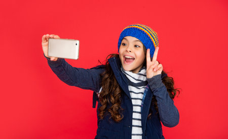 amazed teen girl in down vest with smartphone. portrait of child blogging with phone.