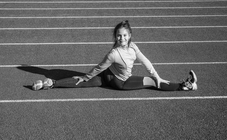 Flexible girl child in sportswear do splits on athletics track, stretching