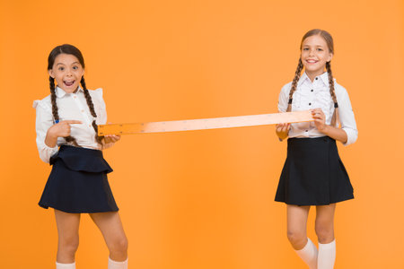 Close or far. Measuring skills. Measuring distance. Measuring equipment. Kids students study math. Knowledge day. Schoolgirls school uniform hold big ruler. Geometry school lesson. Teamwork conceptの写真素材