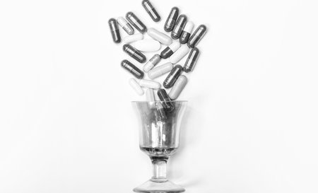 Assorted pharmaceutical drugs pills in capsules spill over glass isolated on white, medicineの写真素材