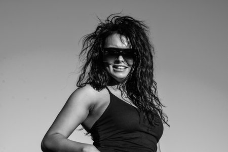 happy brunette woman in sunglasses with brunette curly hair on sky background, summerの写真素材