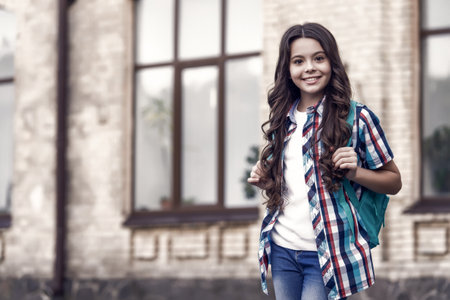 Happy kid with long wavy hair in casual fashion style carry travel bag urban outdoors, travelling