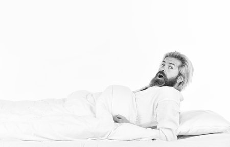 good morning routine. Caucasian bearded guy wearing white bathrobe. relax in a hotel room in a robe. bearded mature man lying on bed at home. Carefree guy enjoying a new day. Morning inspirationの写真素材