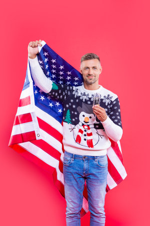 man hold usa flag and champagne in christmas studio. man in christmas sweater holding usa flag.の写真素材
