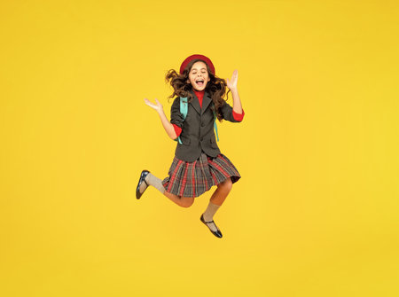 glad teen girl in uniform and beret with school bag running on yellow background, schoolgirlの写真素材