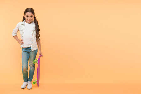 Her favorite activity. Kid girl happy holds penny board. Child likes skateboarding with penny board. Modern teen hobby. How to ride skateboard. Girl happy face holds penny board yellow backgroundの写真素材