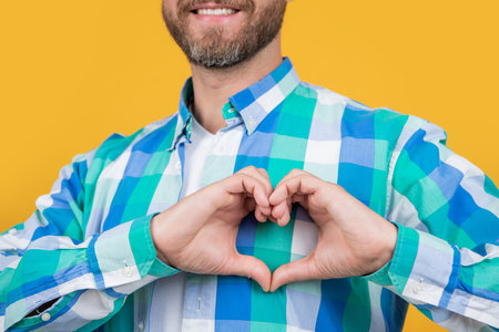 cropped bearded caucasian man in shirt show love heart isolated on yellow background.の写真素材