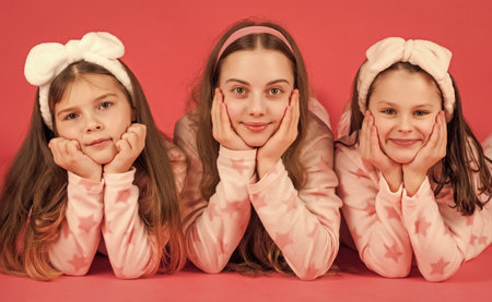 Portrait of happy girls lying with cheeks propped on hands in pajamas pink backgroundの写真素材