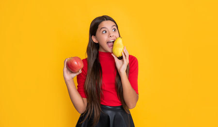 cheerful amazed girl hold fresh apple and pear on yellow backgroundの写真素材