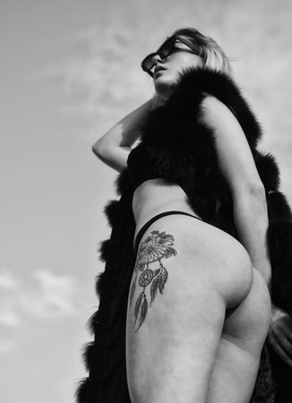 Richness luxury and chic concept. Summer fashion. Tattooed sexy girl. Sexy girl on sky background. Attractive lady sexy body. Risky daring and extravagant. Sexy woman erotic lingerie fur coatの写真素材
